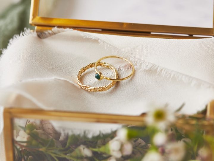 Zwei goldene Hochzeitsringe auf einer weich gefalteten, hellen Stofflage in einer Schmuckbox mit Blumen.