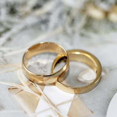 Zwei goldene Hochzeitsringe ineinander verschlungen auf einer dekorativen Unterlage.